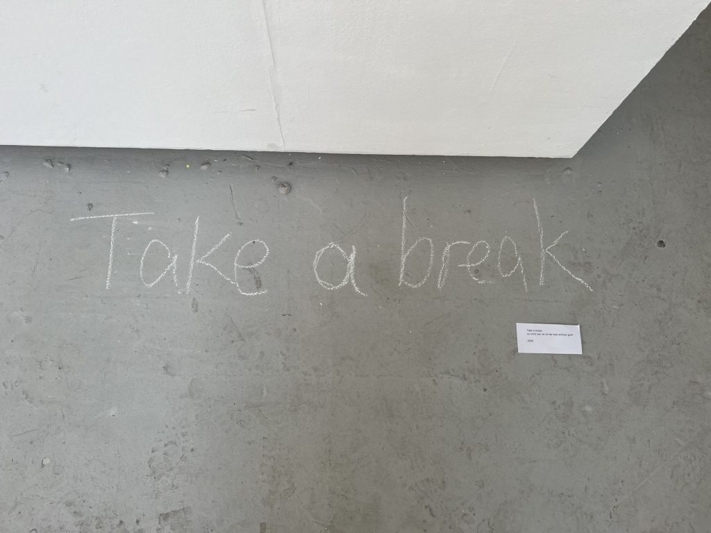 The words 'take a break' written in yellow chalk on a grey floor.