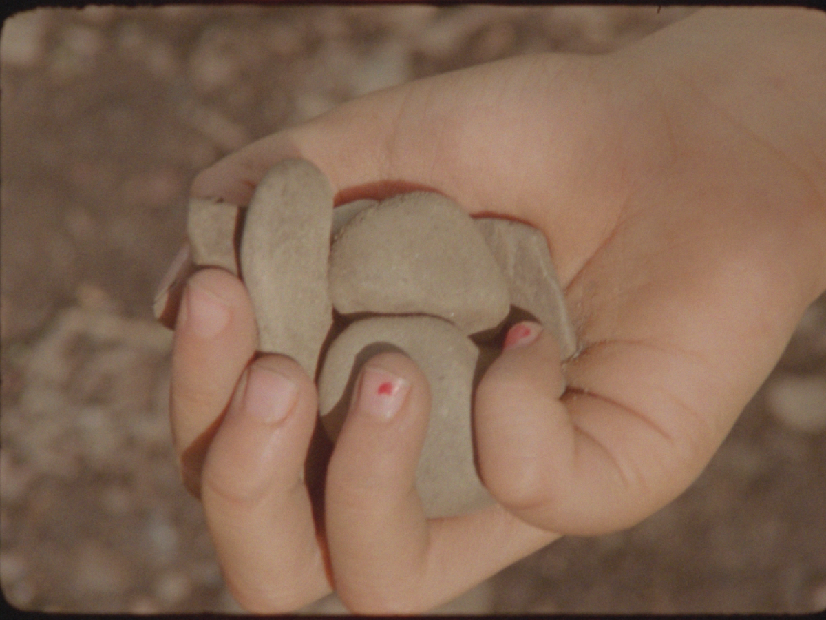 A film still of a hand clutching some pebbles.