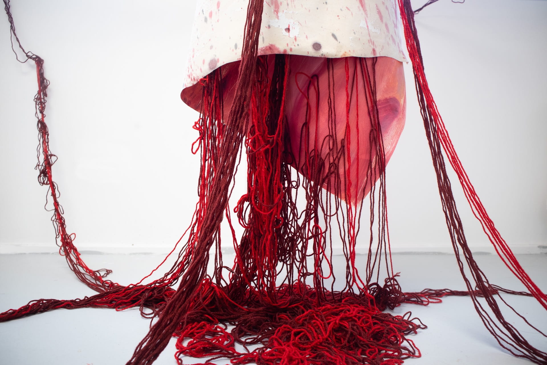 An image of a red sculpture made from wool, hanging in a white room.