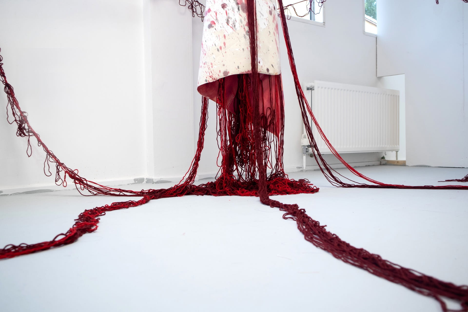 An image of a red sculpture made from wool, hanging in a white room.