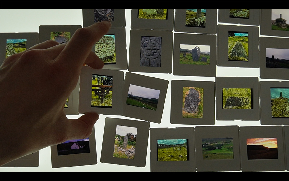 An image of a hand over many 35mm slides depicting carved stone monuments and moss.