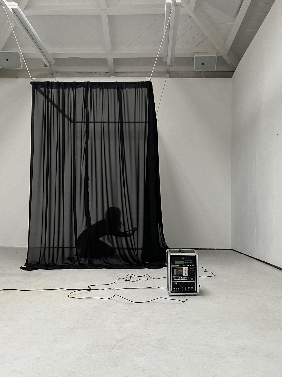 an image of a silhouette of a person crouching inside a black, curtained space, behind an amp.