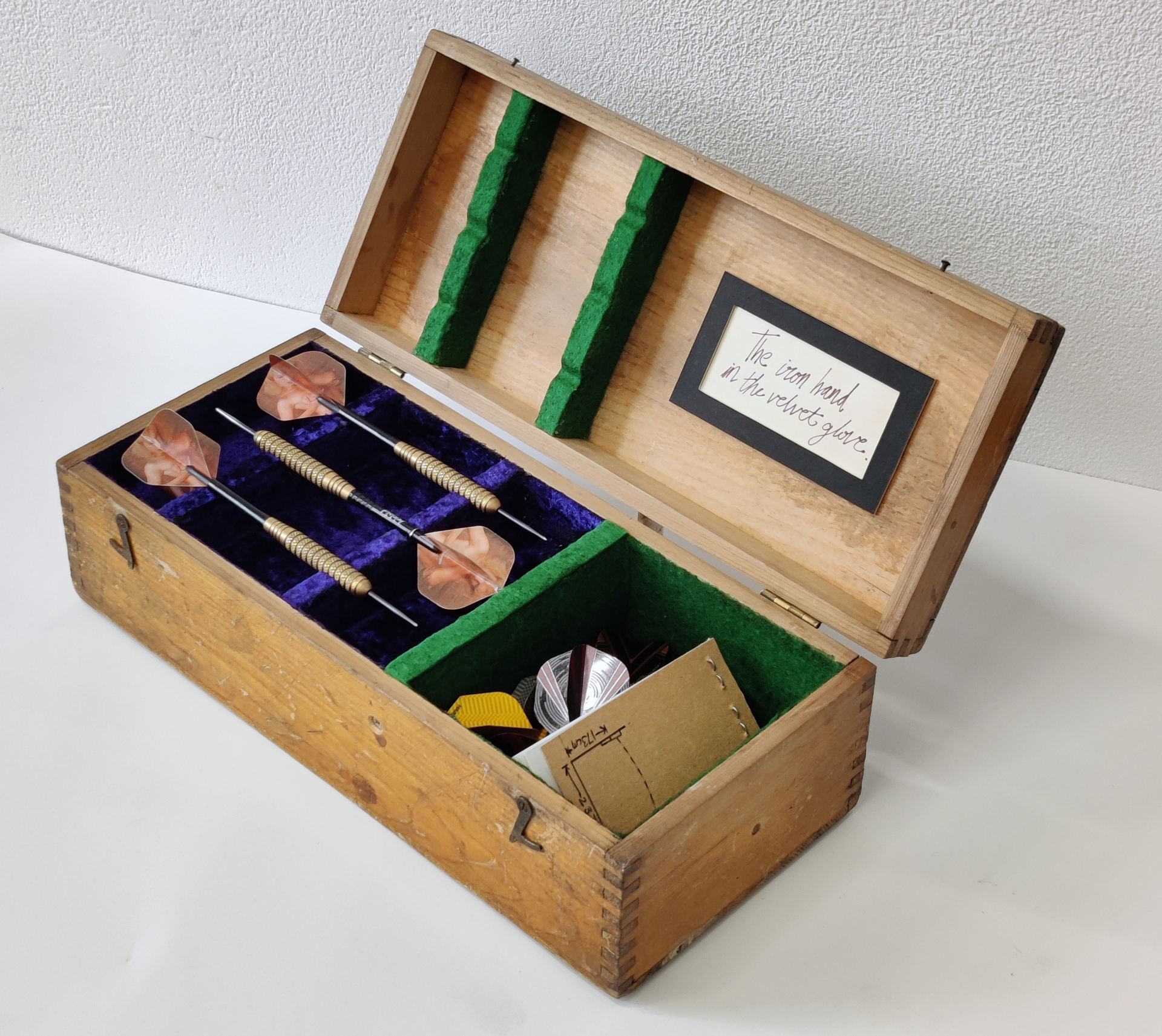 A handmade, velvet and felt lined, dart box. The box holds darts, flights, and notebook, and includes the quote “The iron hand in the velvet glove” on the inside of the hinged lid.