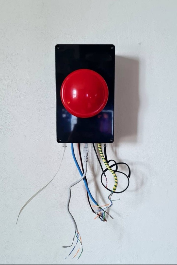 A button both lit up red and unlit on a black electrical box. The wires leading out from it are cut short and knotted. 