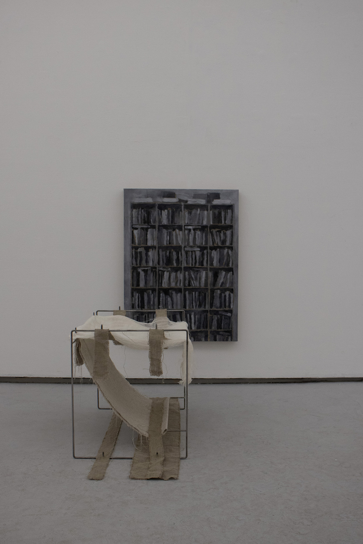 An image of an abstract sculpture in front of a grey painting of books on a bookshelf.