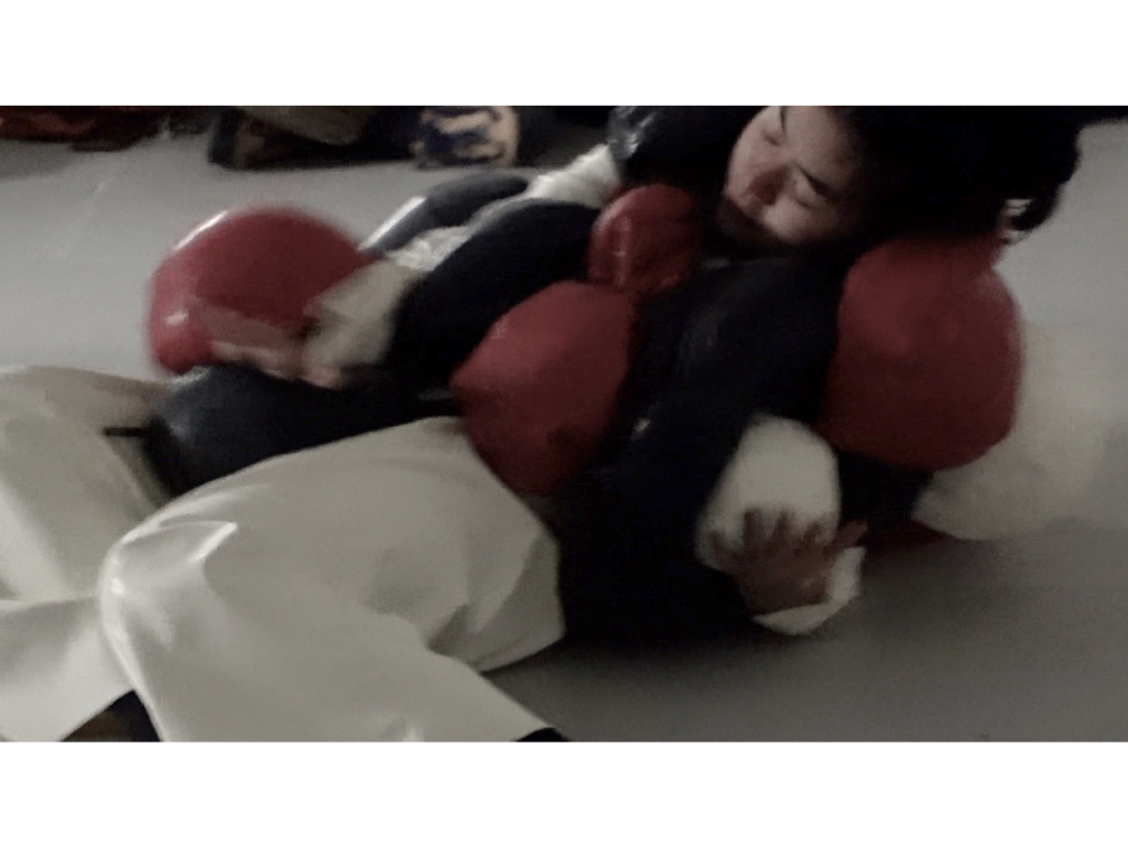 A still from a video where a person is covered in black, red and white balloons.