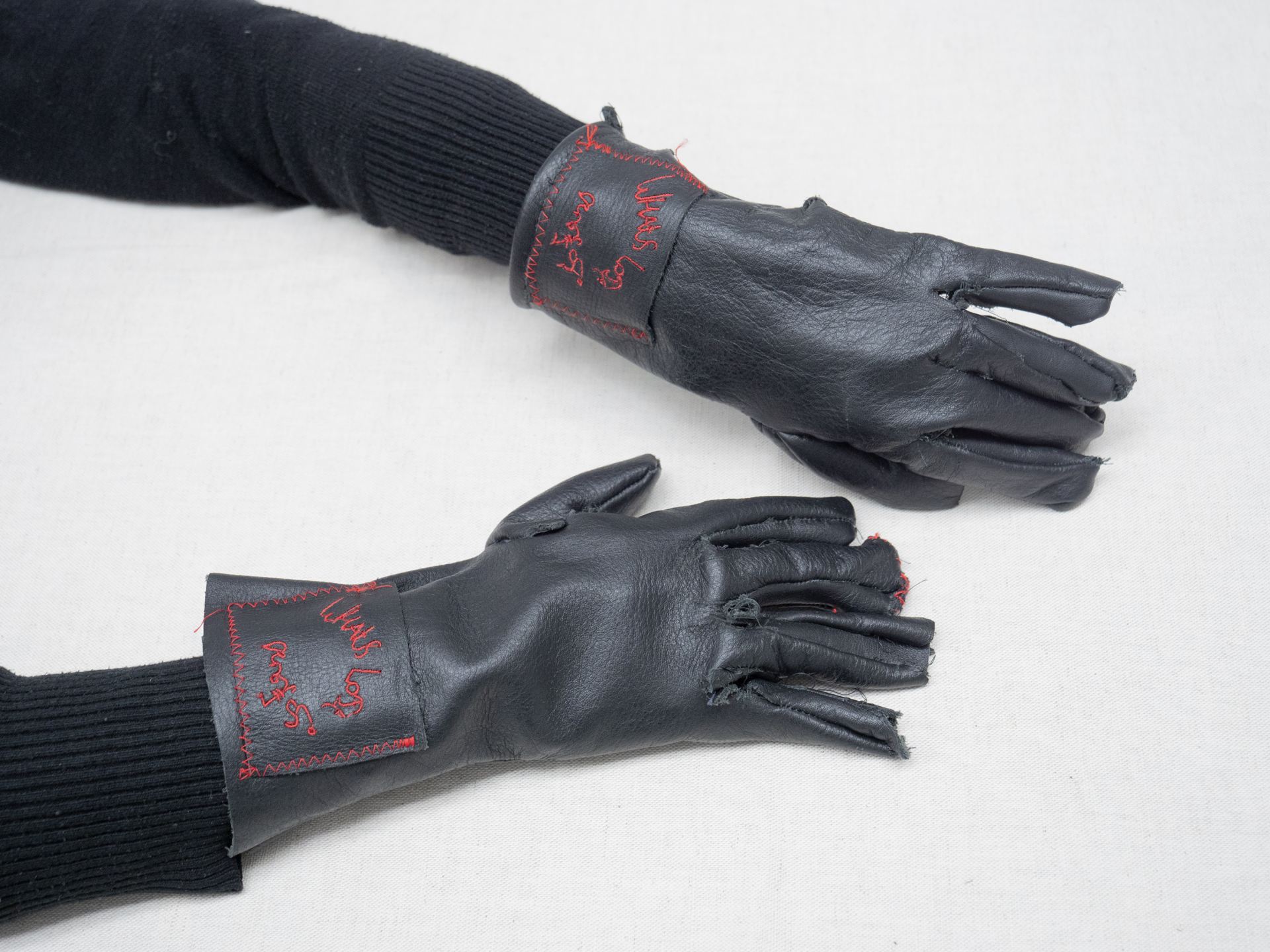 A photo of a person wearing a pair of black leather gloves embroidered with red thread.
