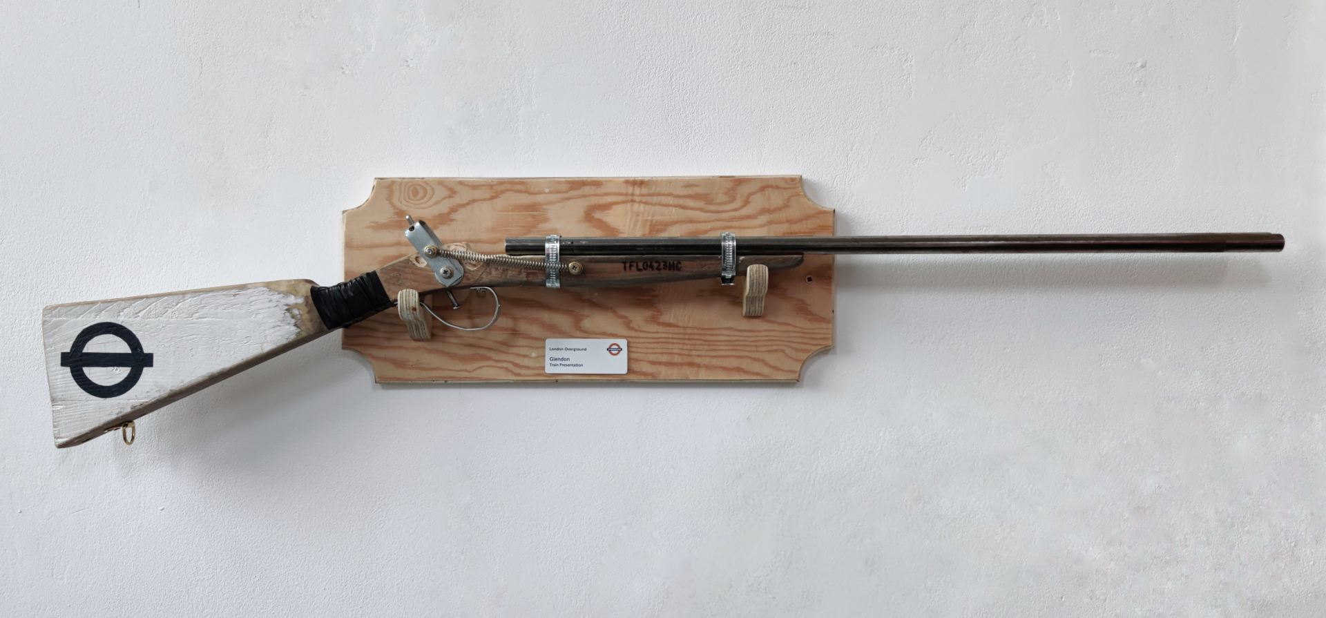 A replica shotgun, made from scavenged materials and hardware, with functional hammer mechanism. Branded with the TFL logo, this prop belongs to an overground staff member named Glendon (as shown on the wall-mounted stand).