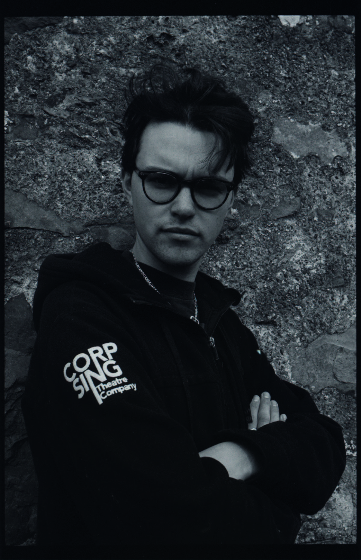 Greyscale photograph of the artist wearing a 'Corpsing theatre Company' branded Jumper.
