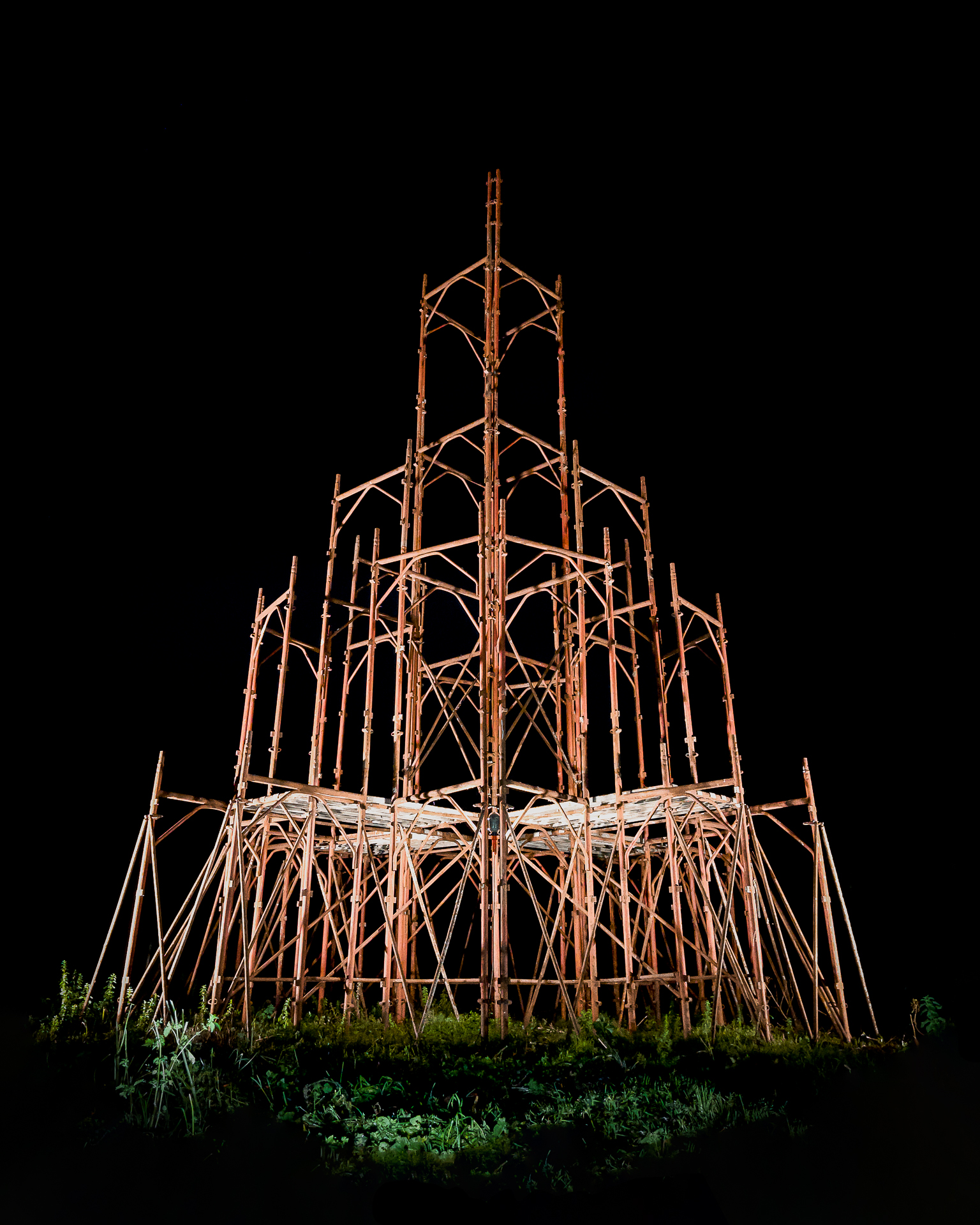 Documentation of a cathedral made from brown scaffolding, against a black background.