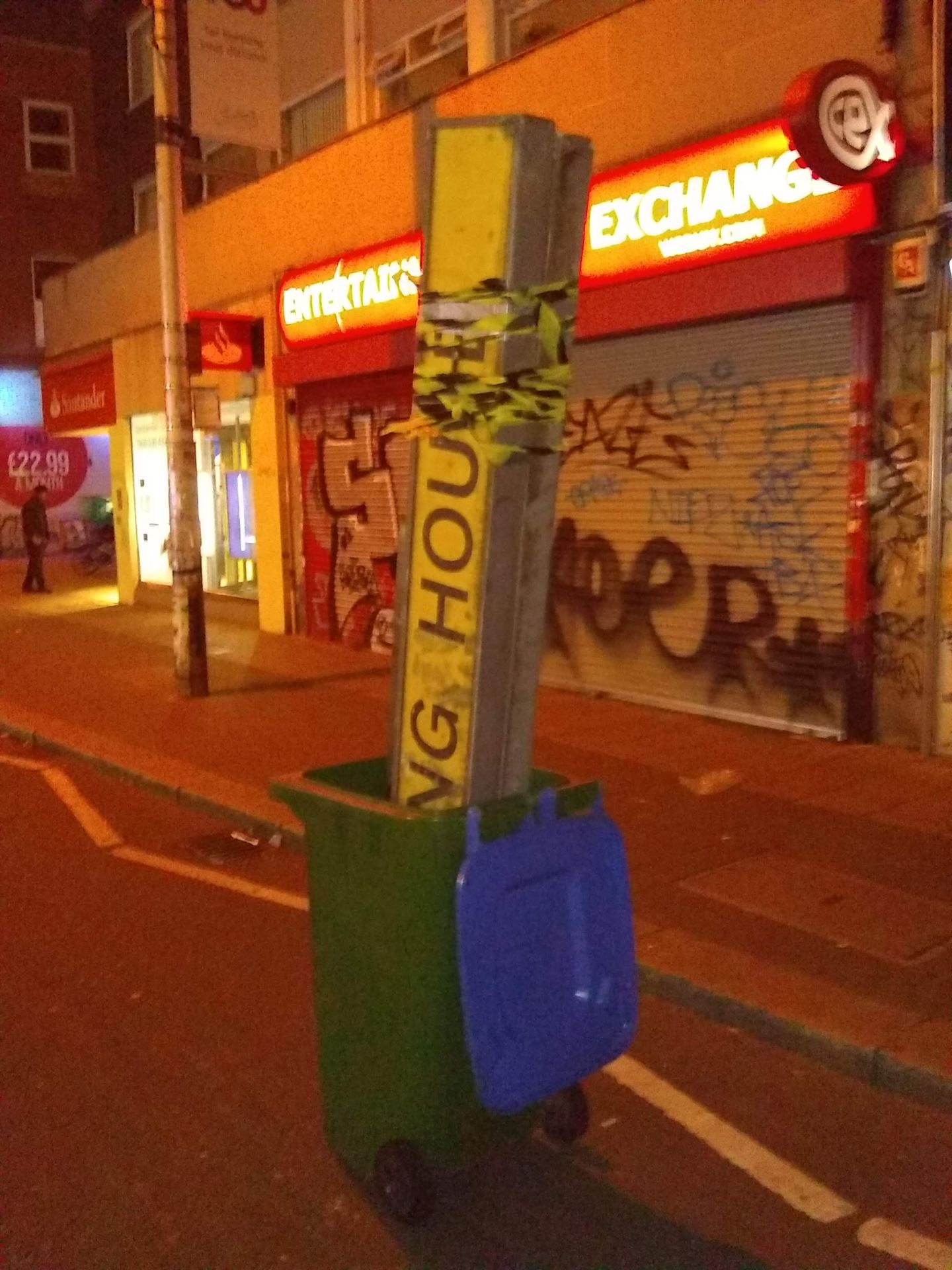 An image of a sign in a green wheelie-bin on a street at night.