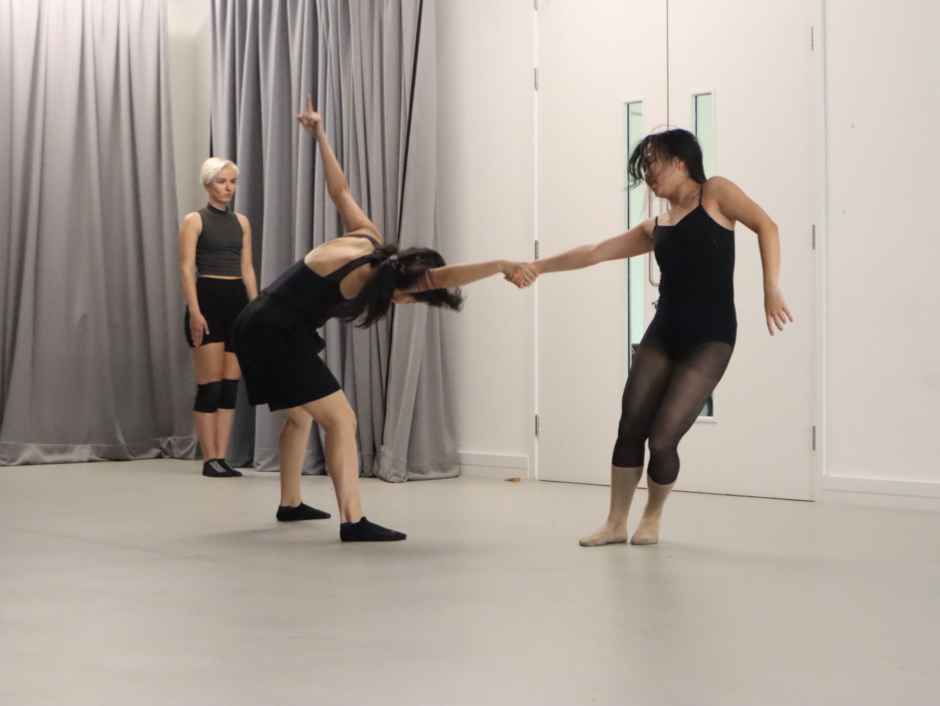 Documentation of three people physically performing in a grey room.