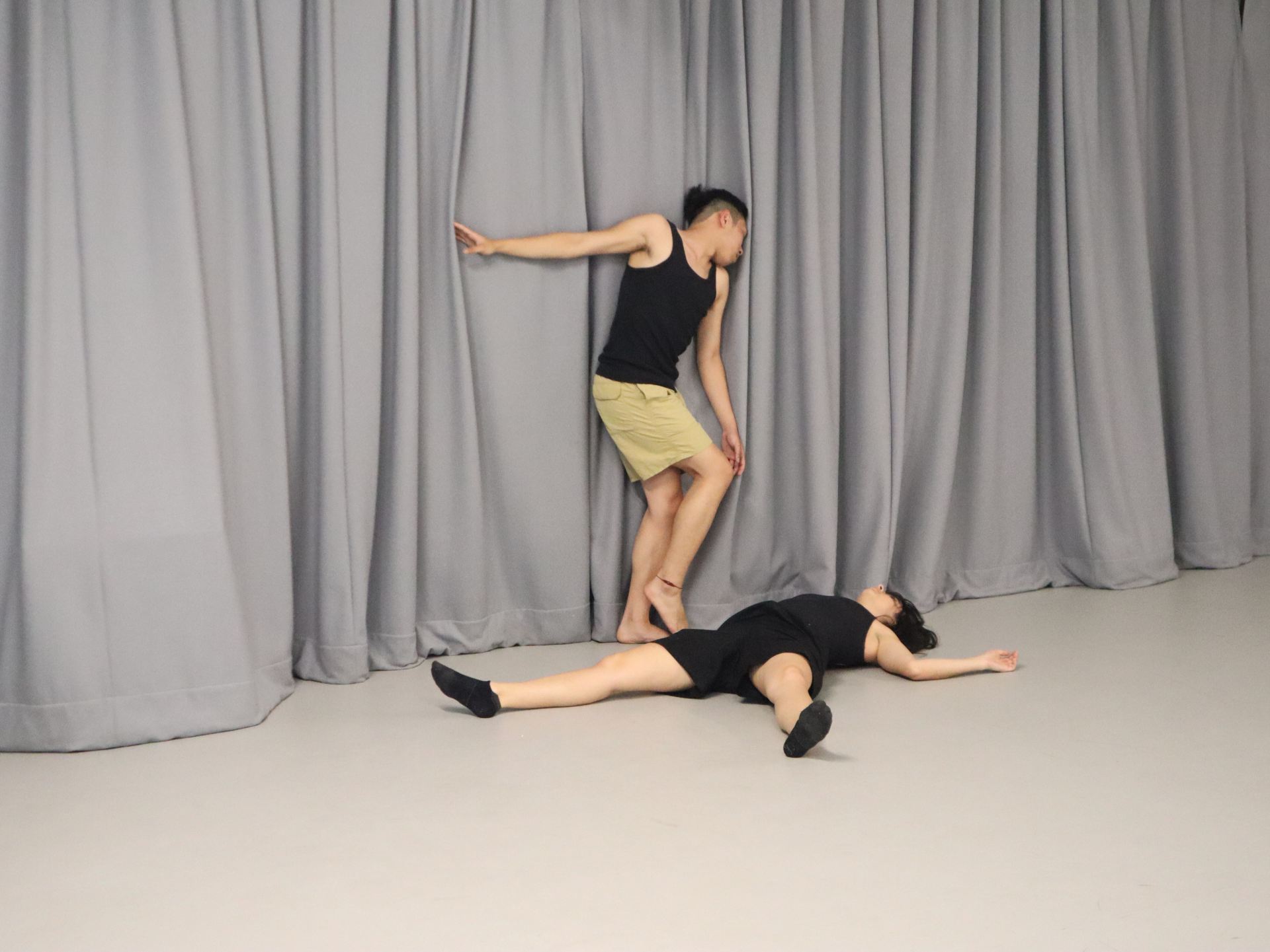 Documentation of two people physically performing in a grey room.
