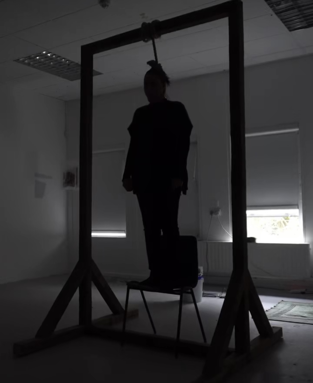 An image of a person stood on a chair with a noose around their neck.