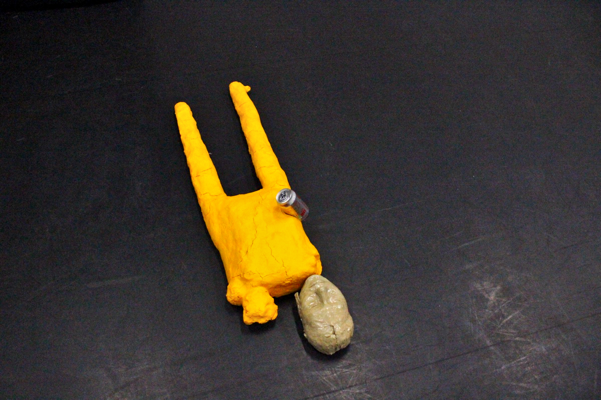 A photo of a sculpture made from yellow and beige found objects, set against a black floor.