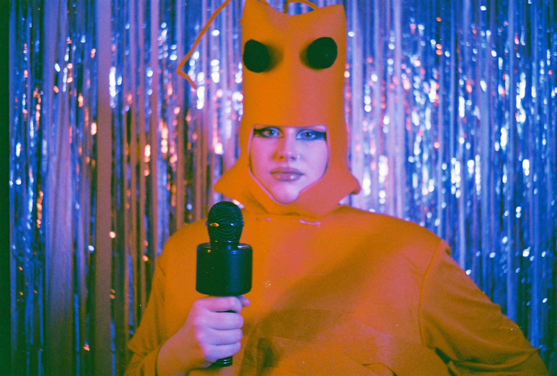 An image of a person dressed as a lobster holding a microphone against a blue background.