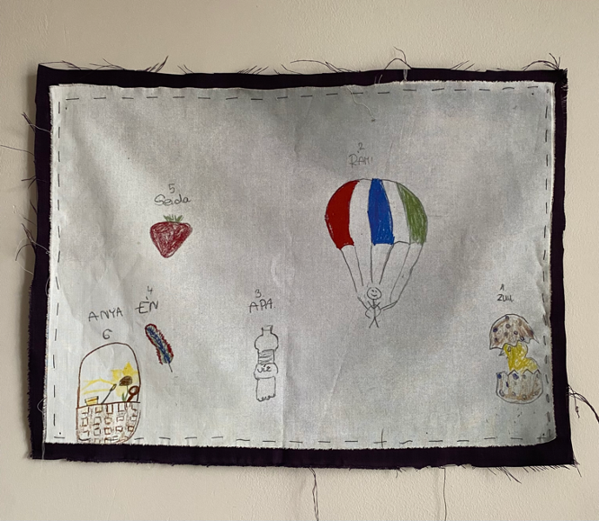 An image of a child's drawing of a family sewn onto black fabric.