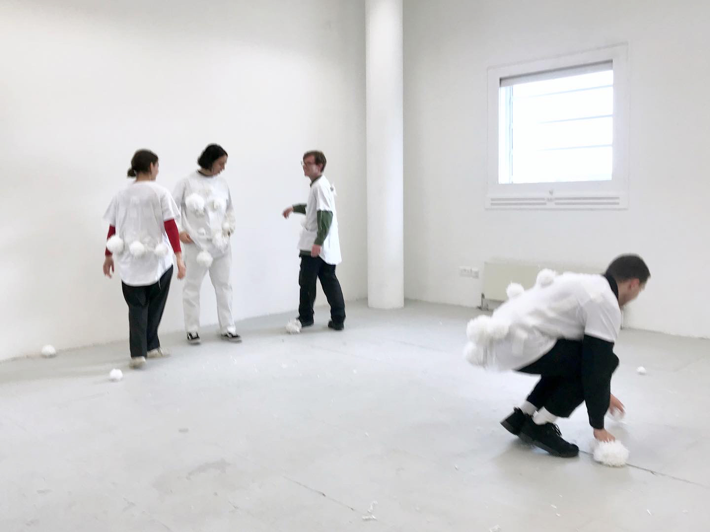 An image of several people participating in a snowball fight with wooden balls, by wearing white, velcro t-shirts, in a grey room.