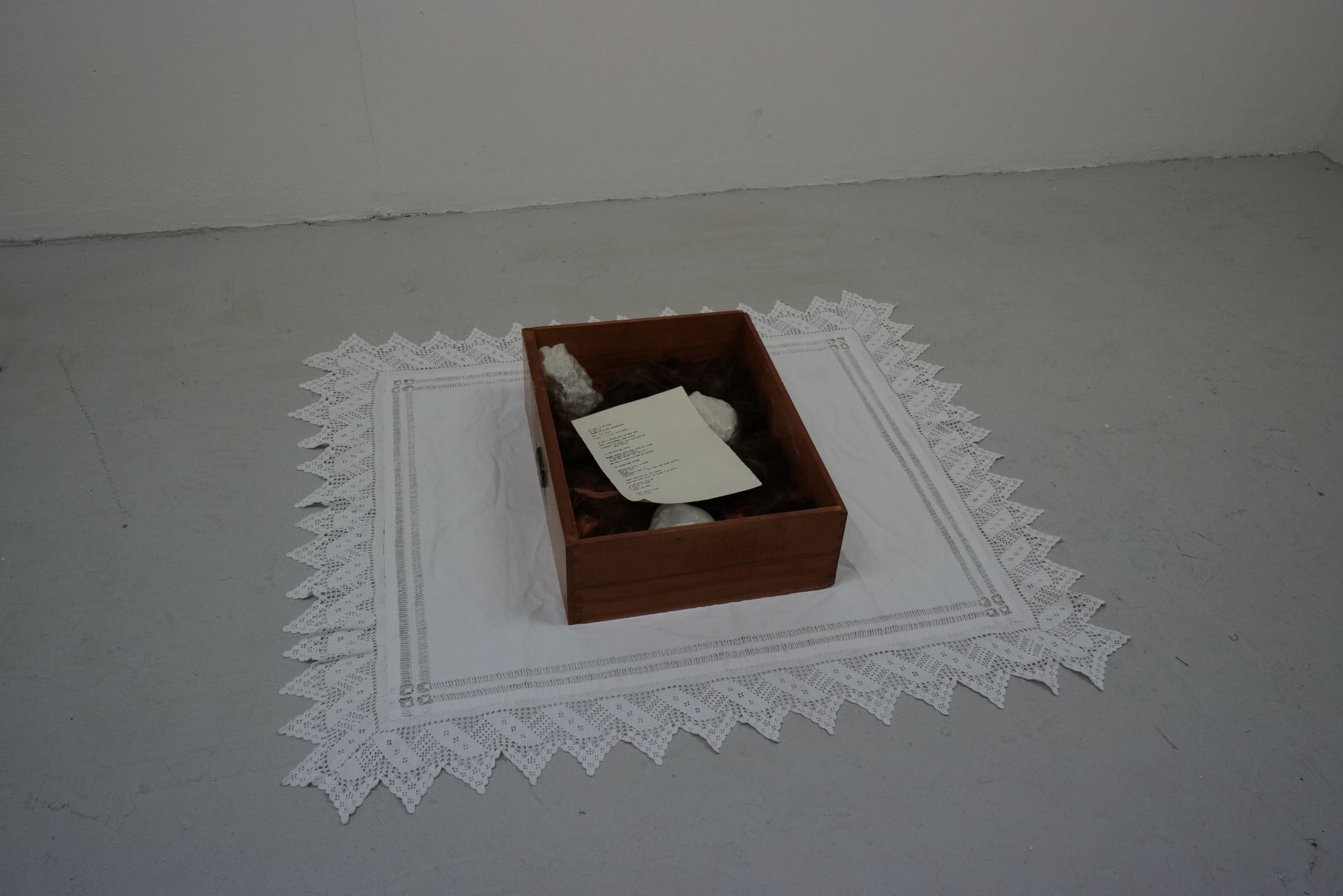 A bird's eye view of a box containing 3D printed stones and a handwritten note. The box is sitting on a white tablecloth.
