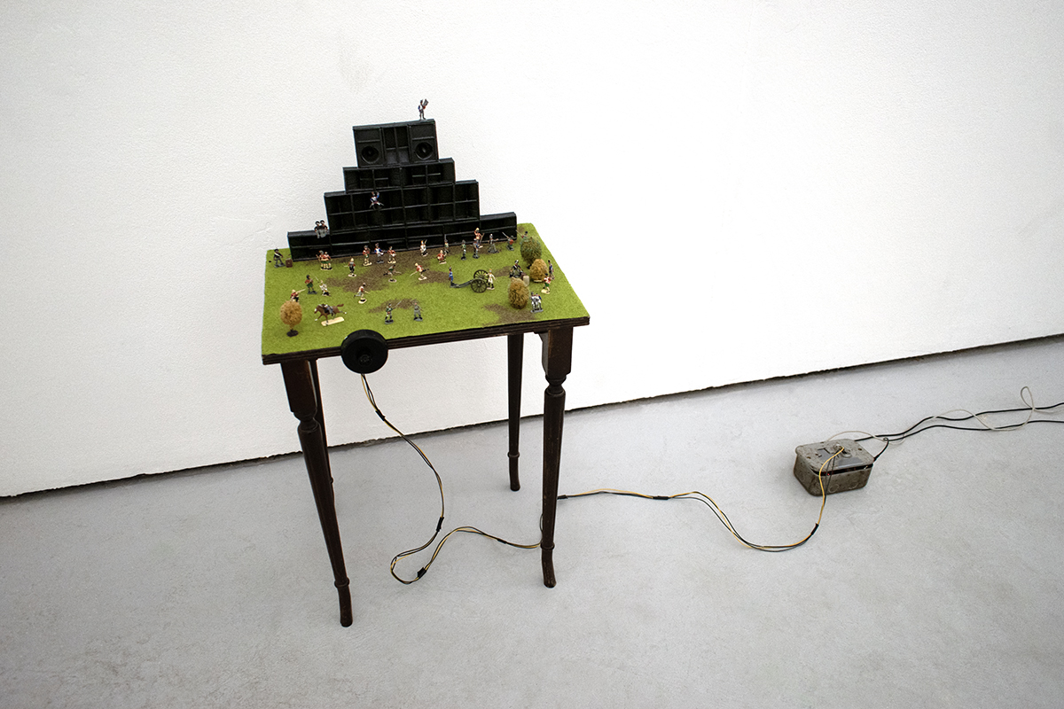 Diorama of a sound system with army figurines. A distance reactive bass tone gets louder as the viewer walks toward the model.
