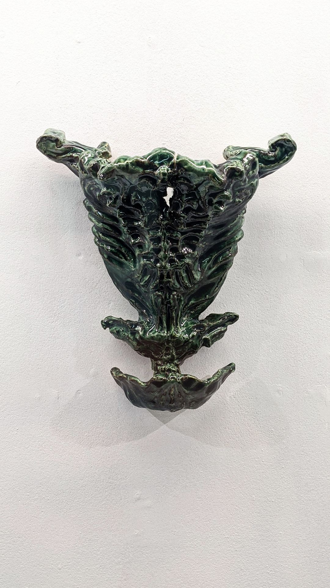 An image of a curvy, green ceramic object hung on a white wall.