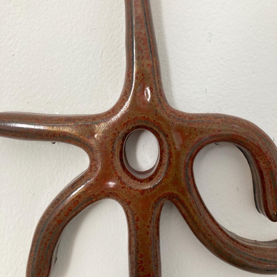 An image of a rust red ceramic hanging on a white wall.