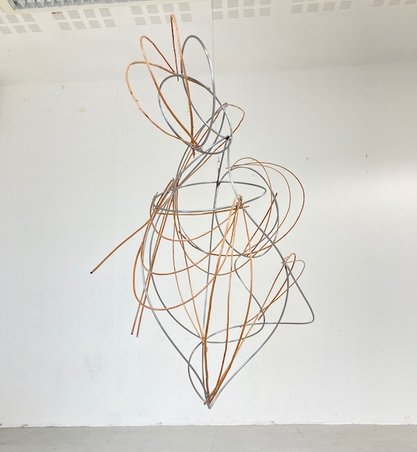 An abstract sculpture made from bent and spiralled steel, mimicking the external fluidity of willow and internal potential for
the life of metals. It is hanging against a white background.