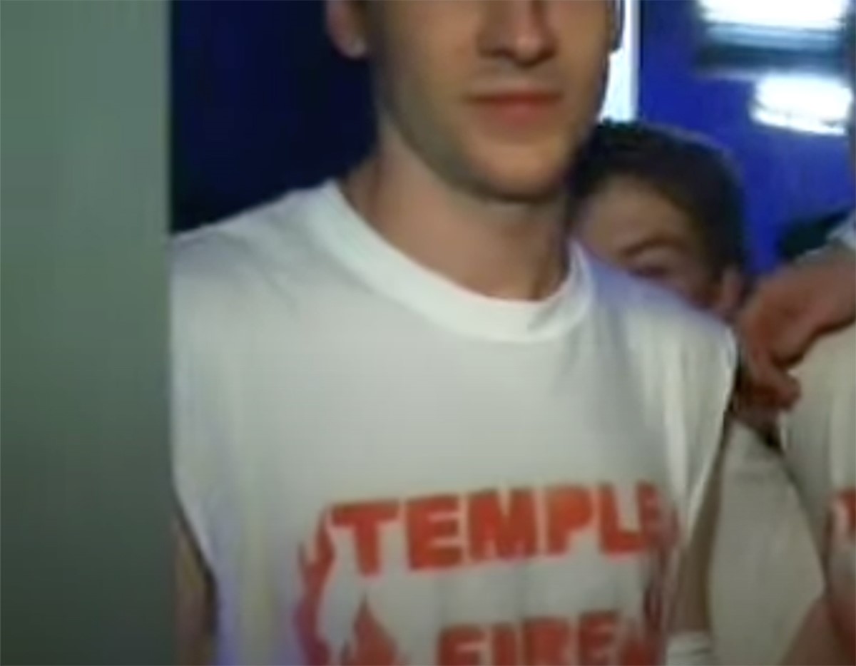 A low res photo of the chest of a man wearing a white t-shirt that says 'TEMPLE'.