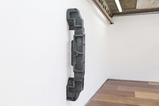 A grey sculpture hing on a white wall.