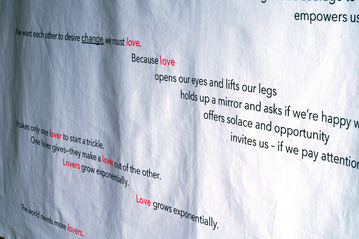 A red and black piece of text about love printed in ink on raw canvas.