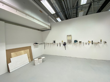 An image of a room with plywood stacked against a wall, and tools hung in a line on another wall.