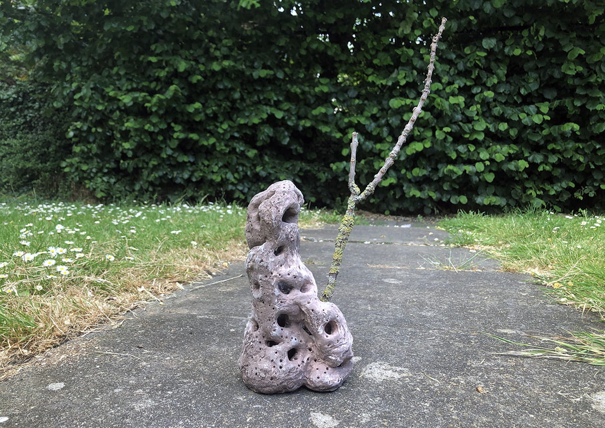 An image of a grey ceramic sat on a path in front of a hedge.