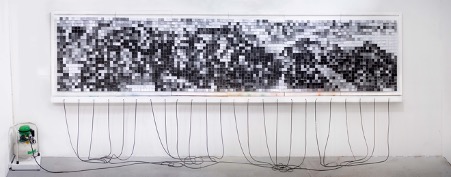 An image of a black, white and grey pixellated rectangle ing on a walll and attached with multiple tubes to an air compressor.