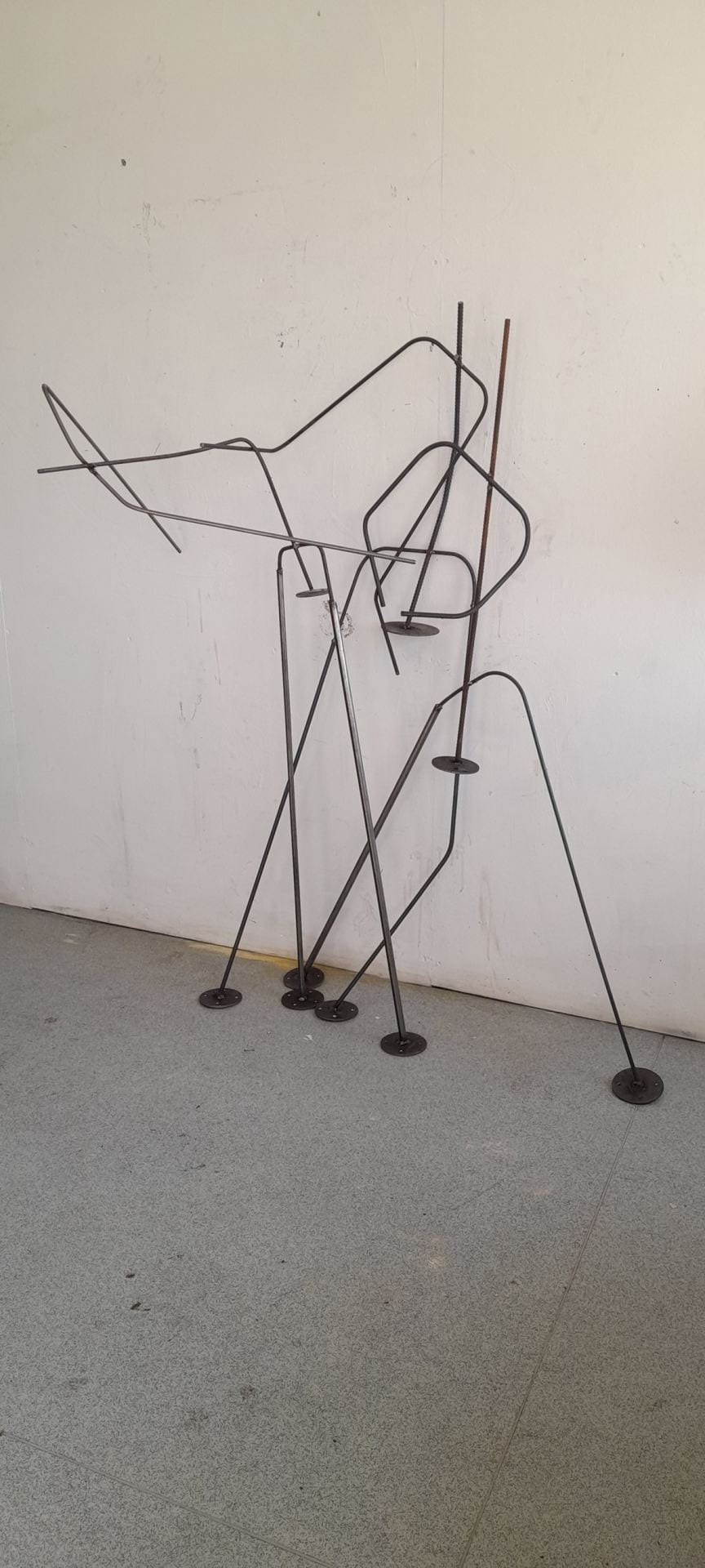 An image of pair of abstract figures made out of metal rebar leaning against a white wall.