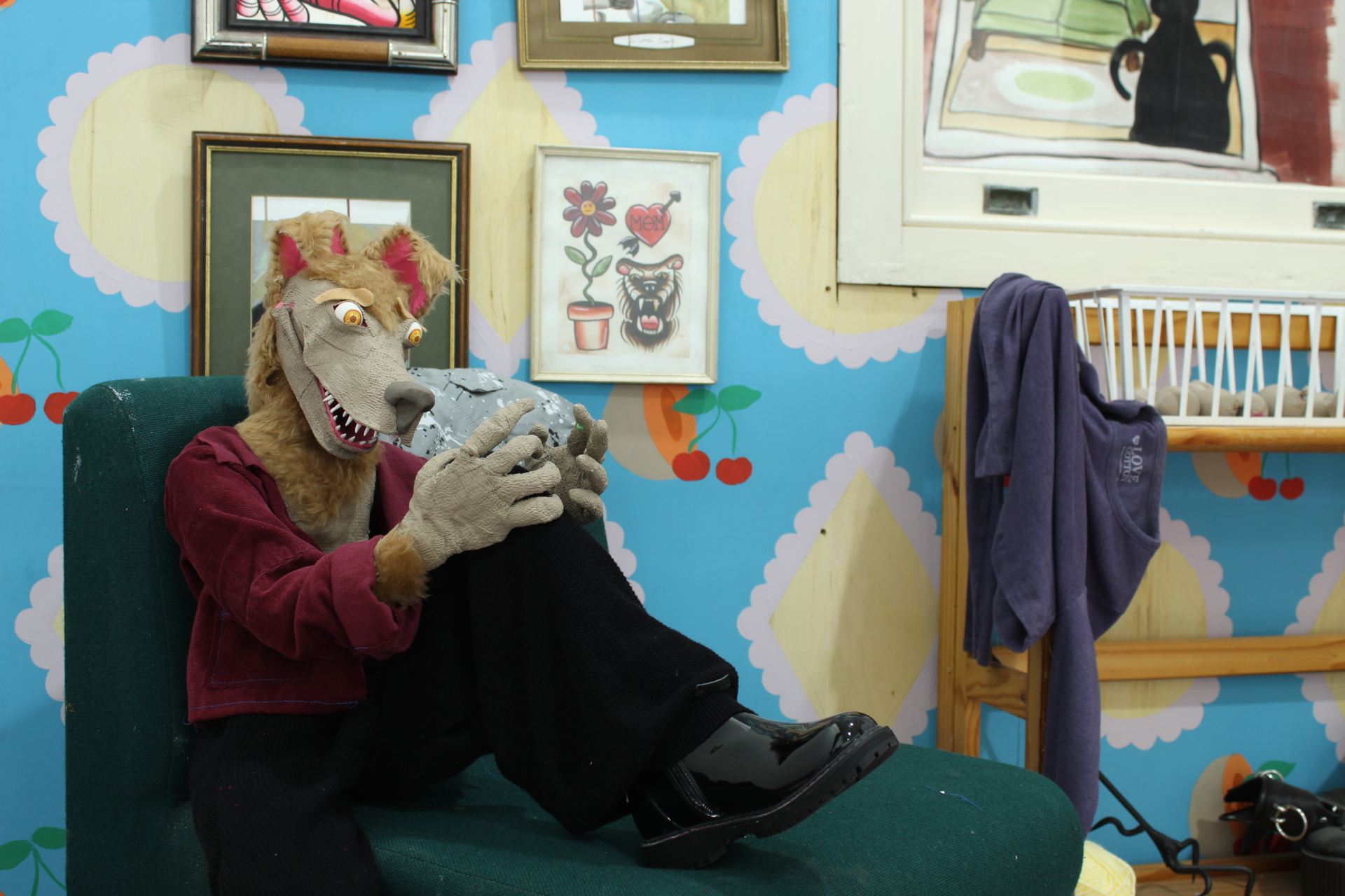 A wolf puppet sits nervously in a colourful room with his hands resting on his knees.