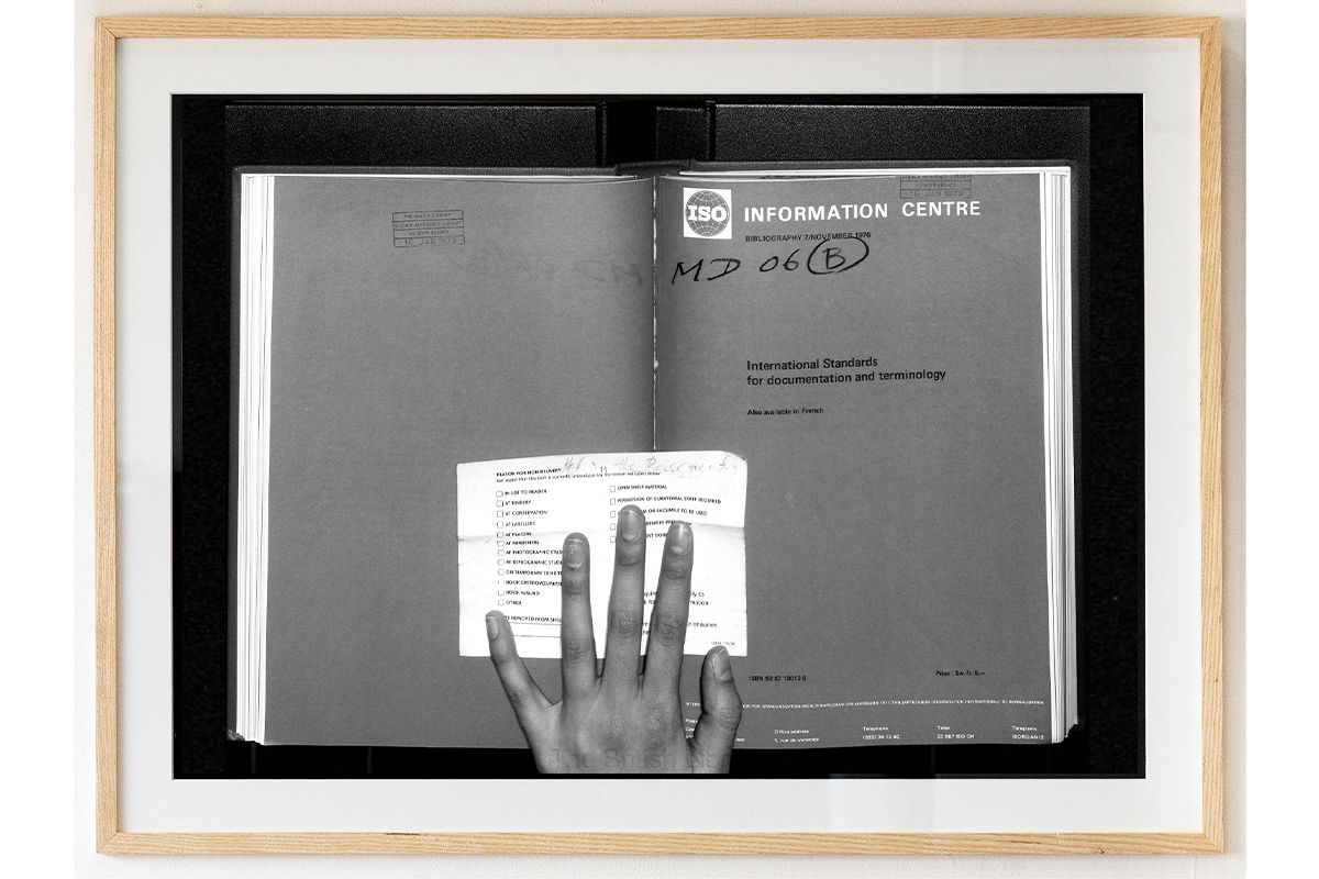 A greyscale image of a hand over a textbook, in a light wooden frame.