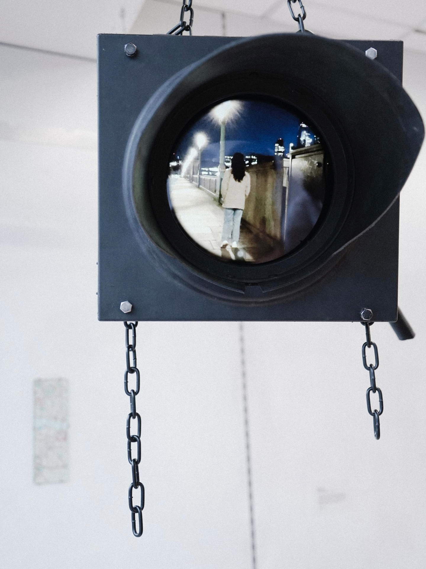 An image of a video screen inside a repurposed traffic light, hanging from black chains in a white room.