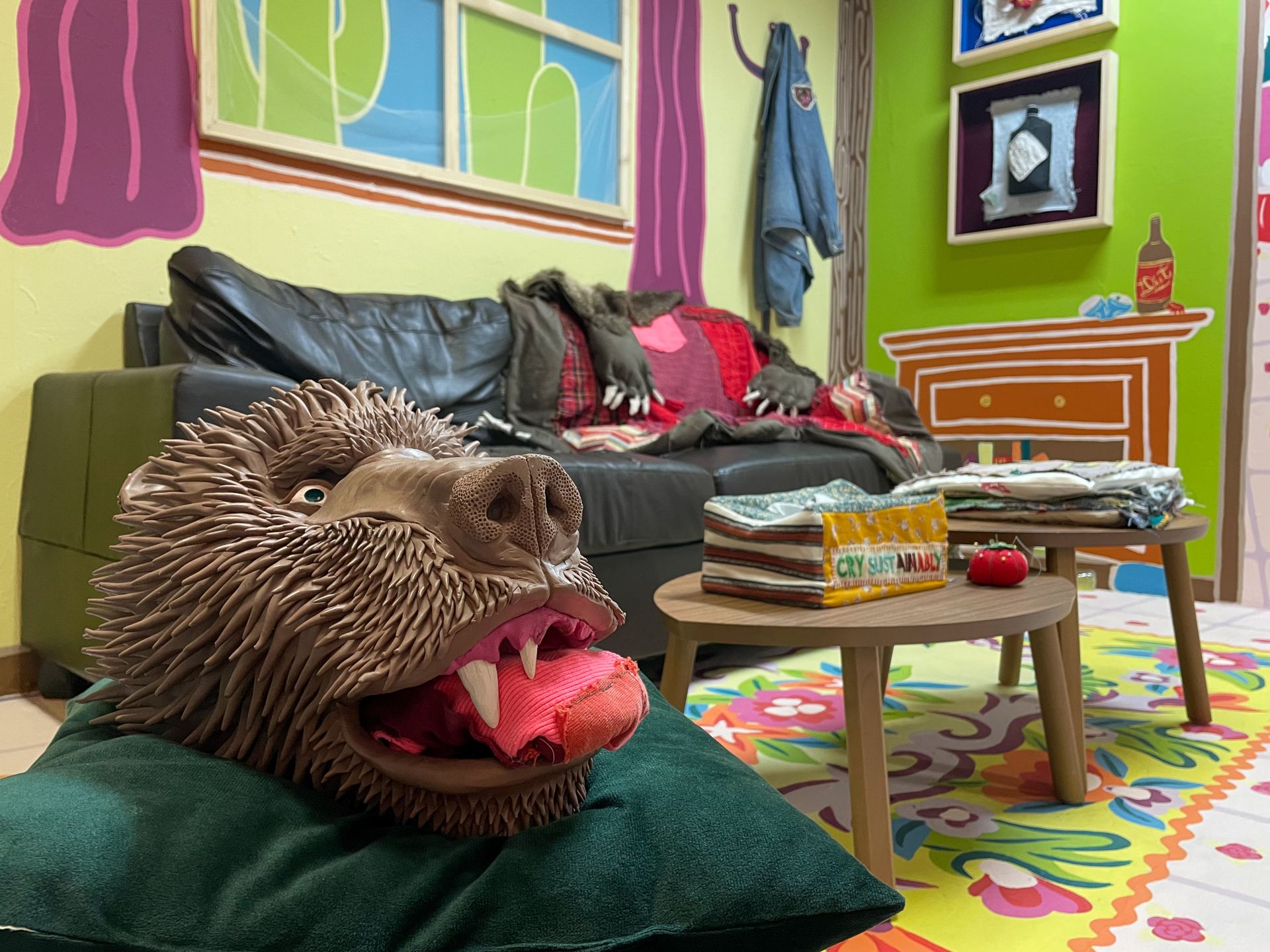 A clay bear head rests in the foreground with a colourful room behind him.