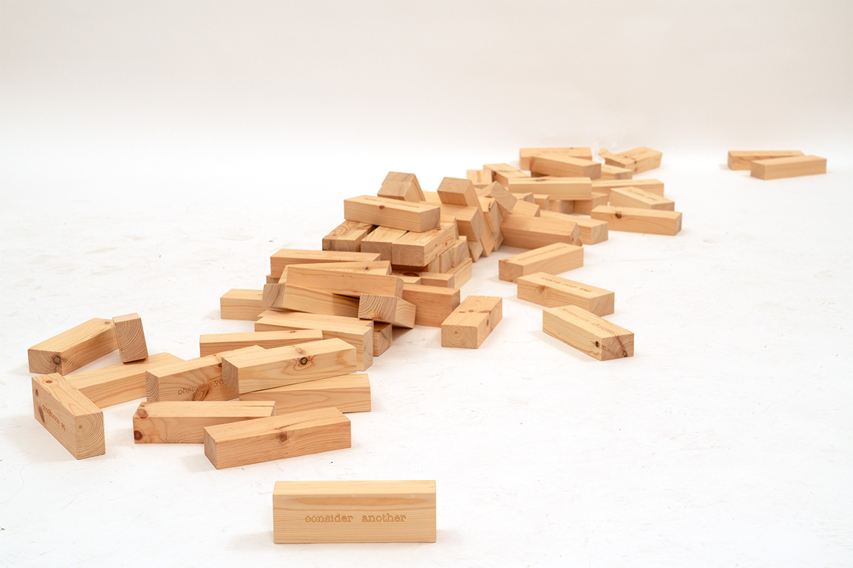 A plinth-like pedestal made of wooden, inscribed blocks stacked like a jenga game against a white background.