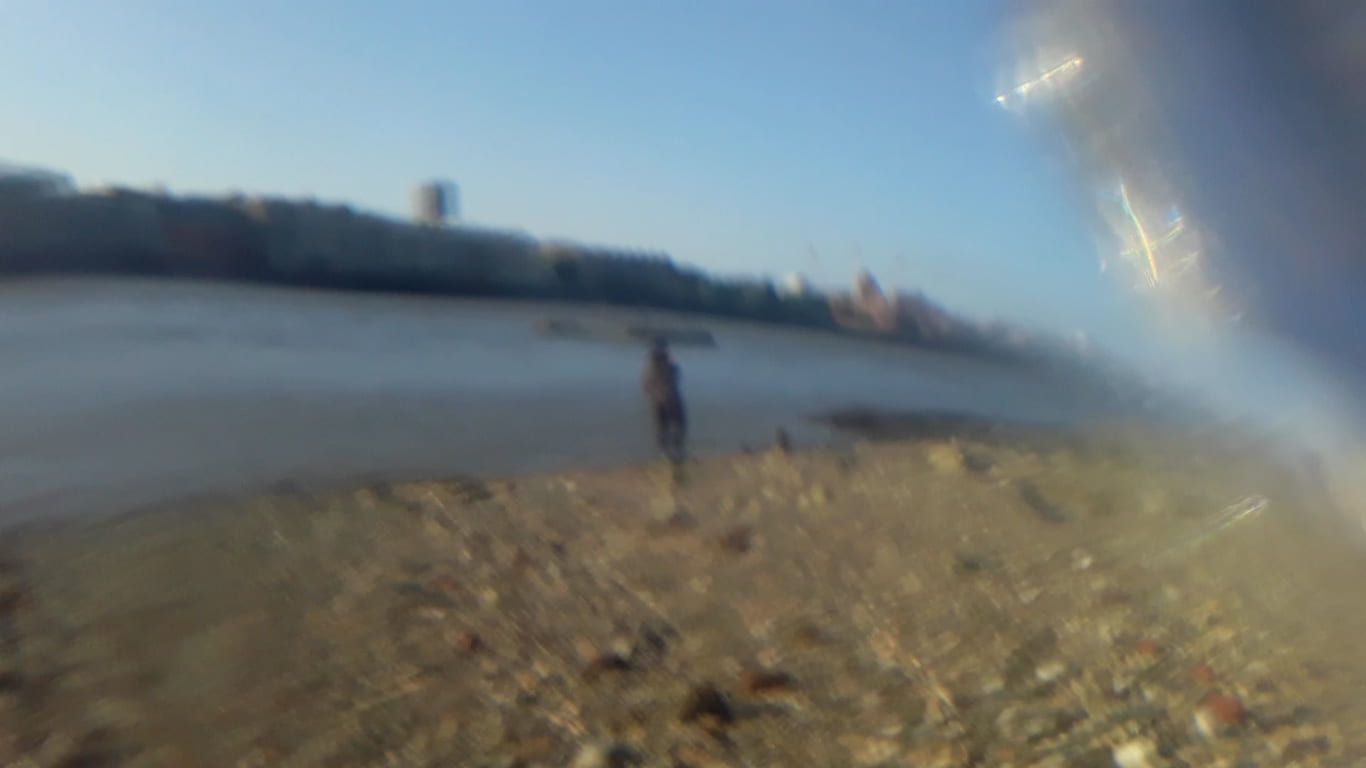 A blurred image of a person standing on the Thames foreshore.