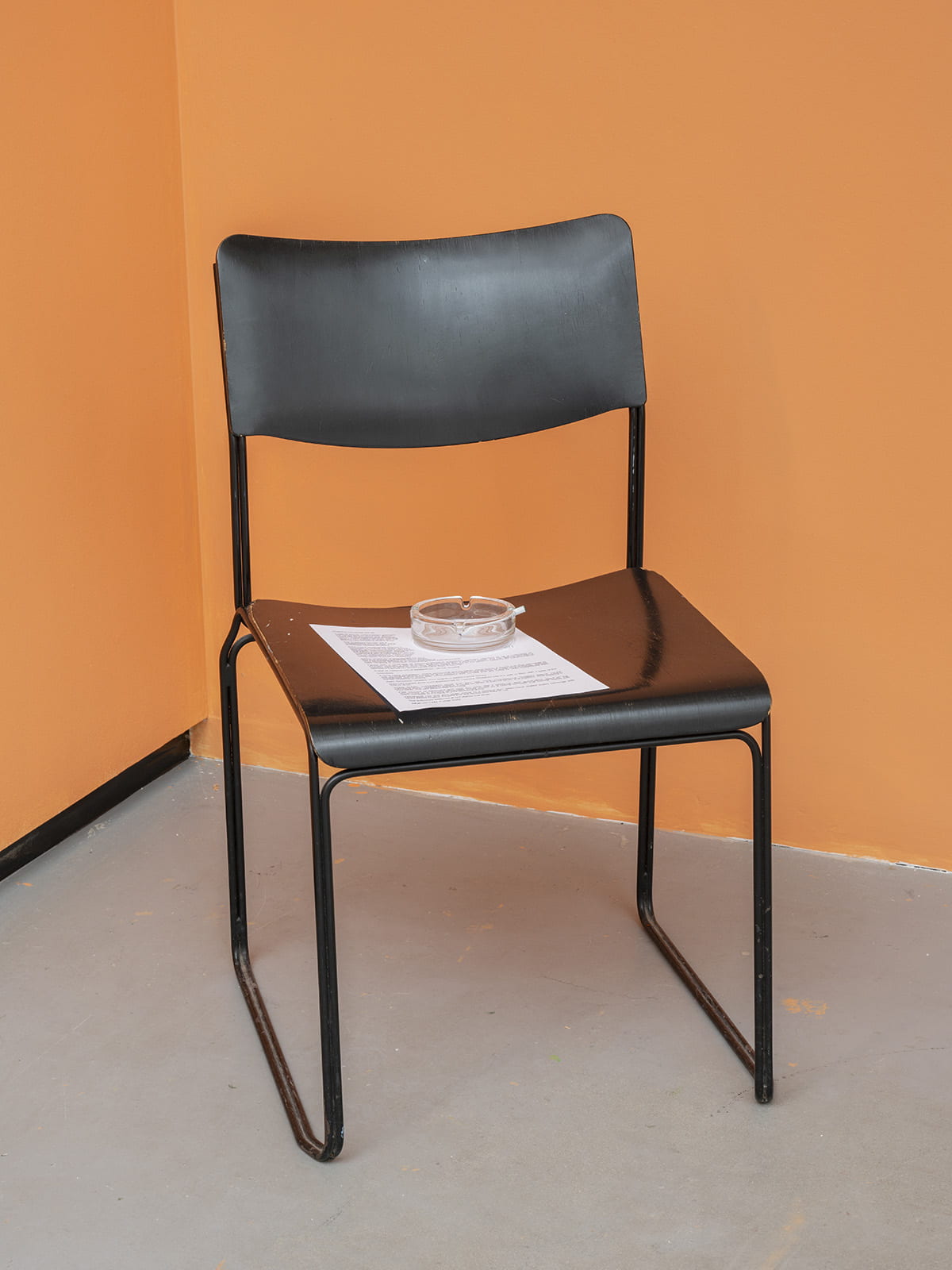 An image of a chair upholding a piece of typed paper, an ashtray and a cigarette.