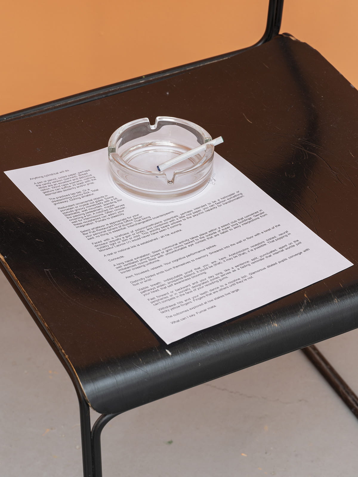 An image of a chair upholding a piece of typed paper, an ashtray and a cigarette.