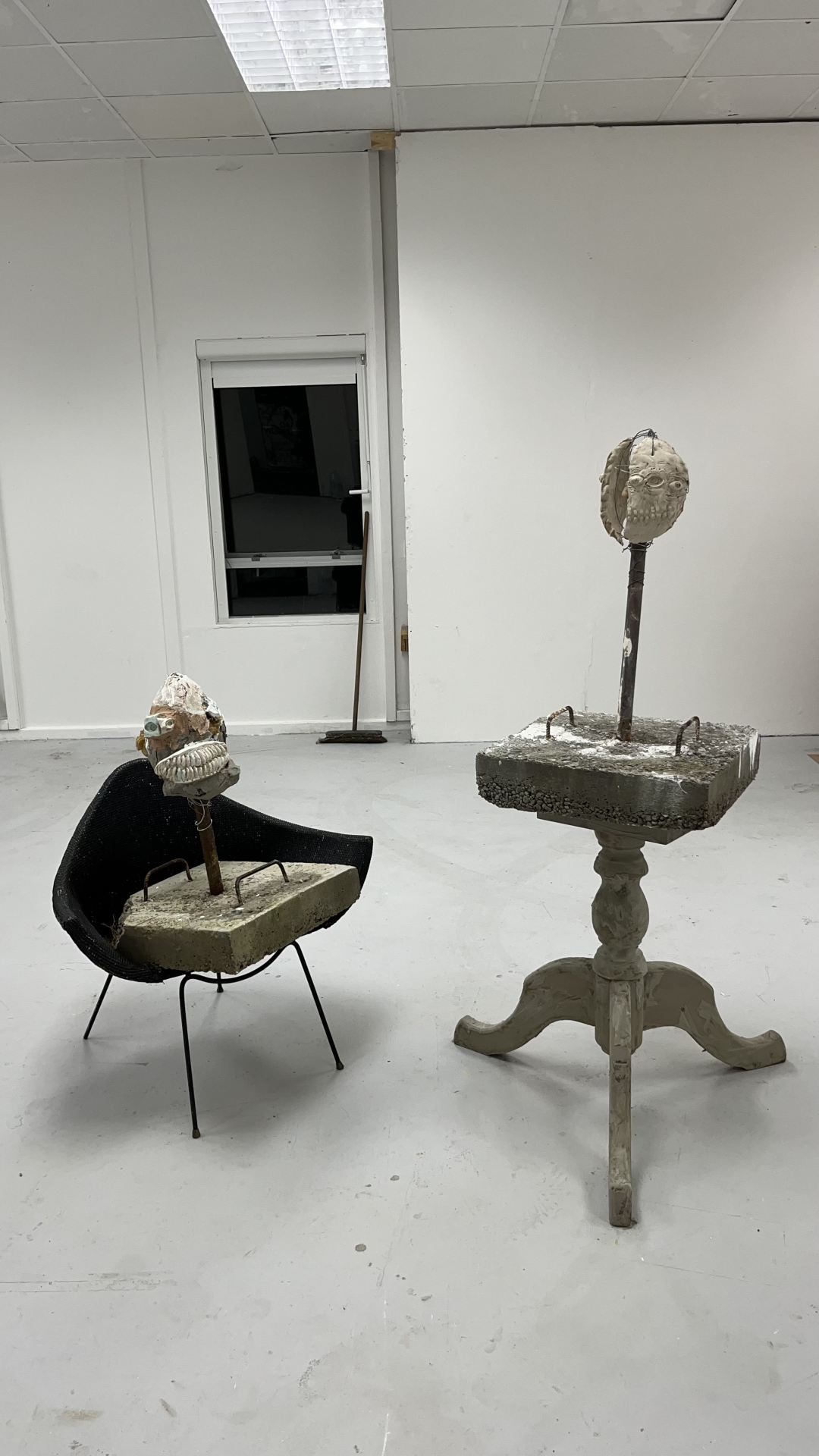 An image of two figurative sculptures standing in a grey room.