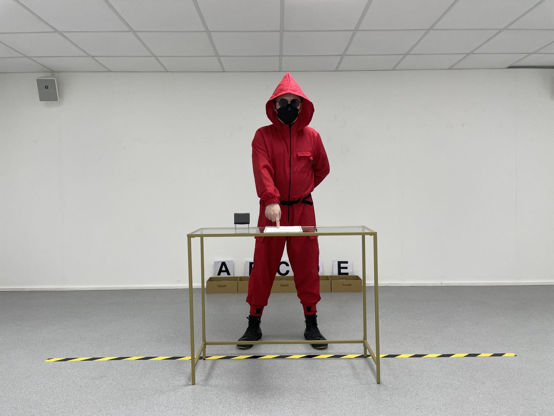 An image of a person in a red costume standing next to a glass table.