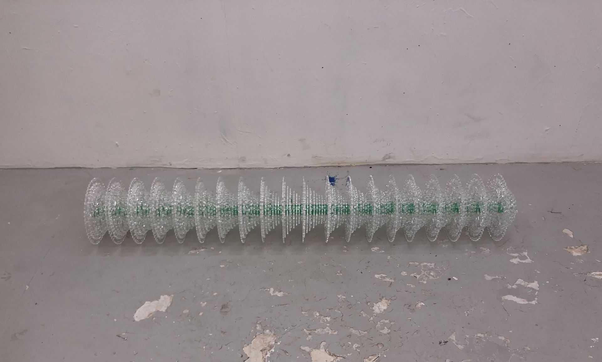 A transparent, cylindrical sculpture lying on grey floor.