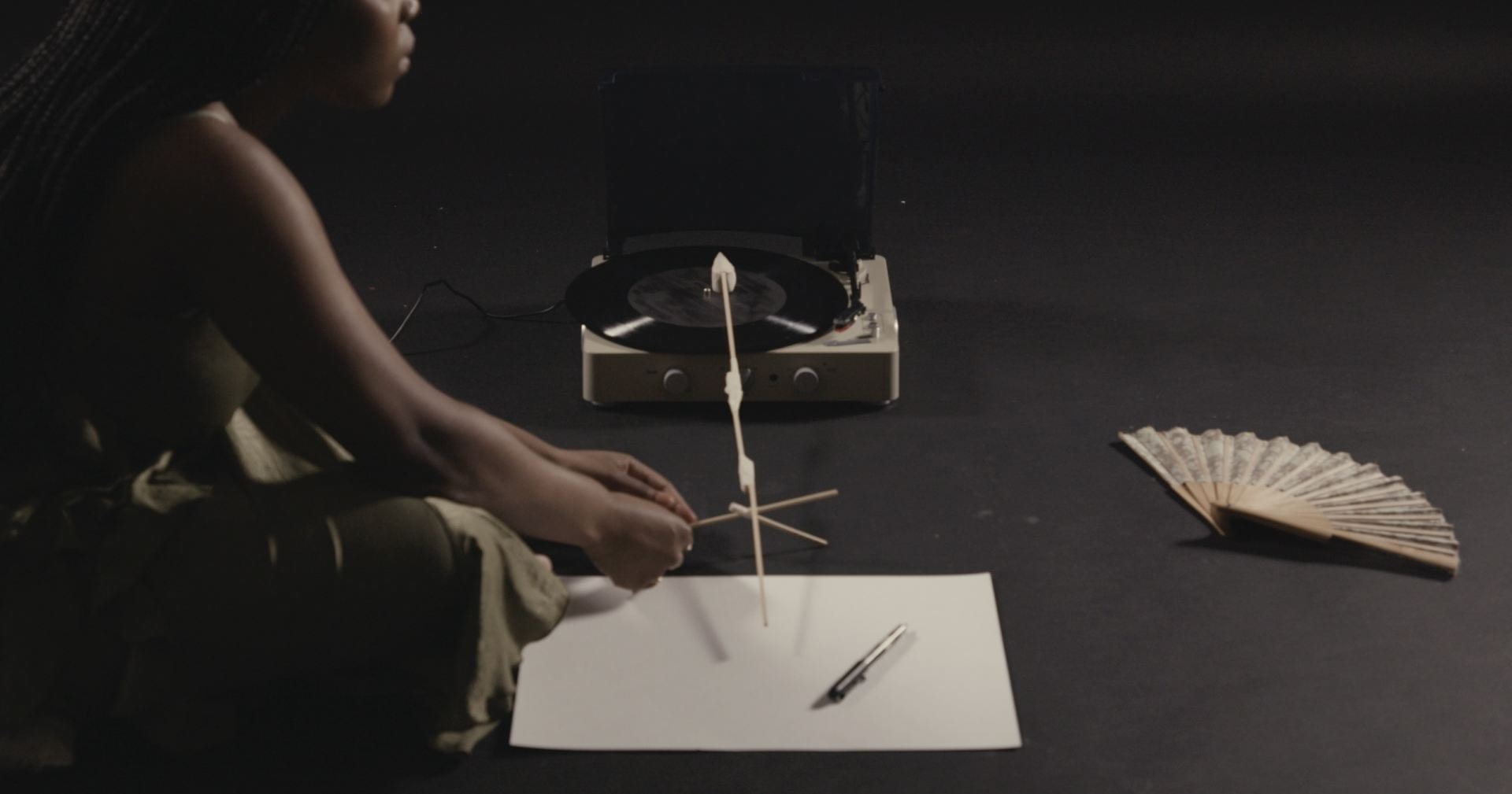 An image of a person sitting cross-legged with an elaborate drawing utensil in a dark room.