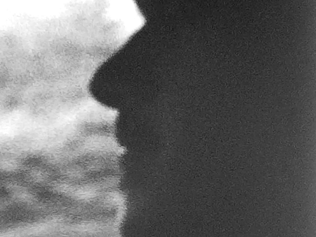 A black and white film still of a profile of a face.