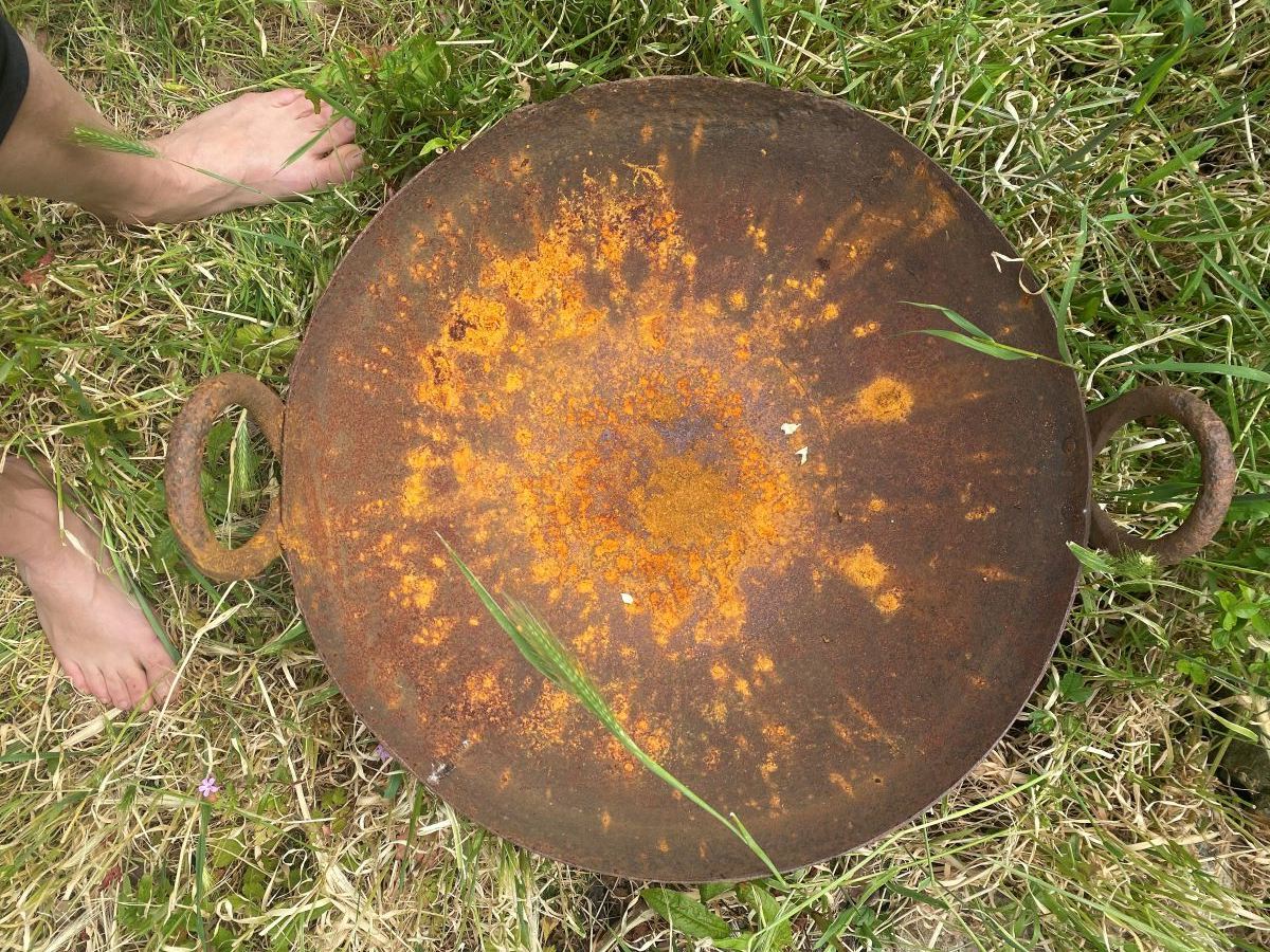 An bird's eye view of a person's feet and a rusting, are bowl set on some grass.
