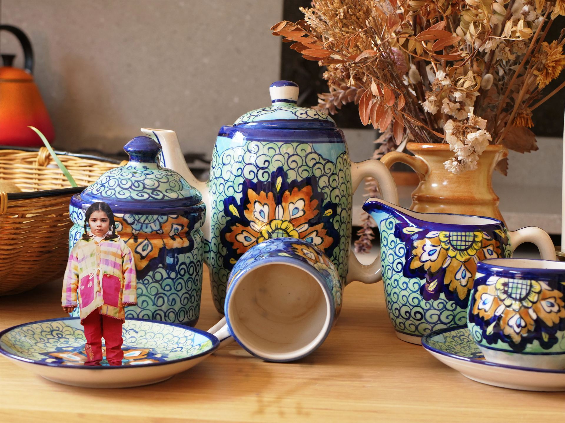 An image of a child juxtaposed amongst an ancestral ceramic tea set in a domestic setting.
