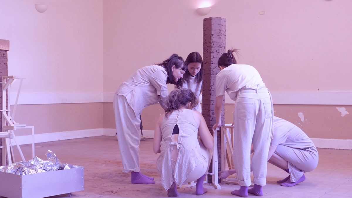 An image of several people building a column in a pink-tinted room.